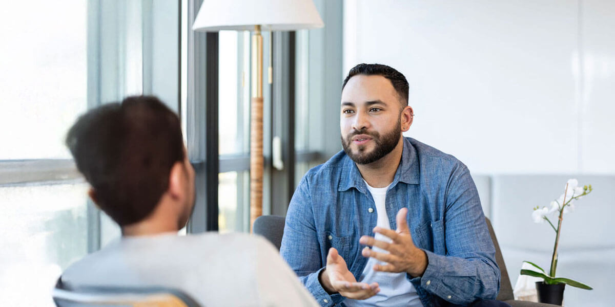 A young male therapy patient gestures as he talks about something with a female therapist.