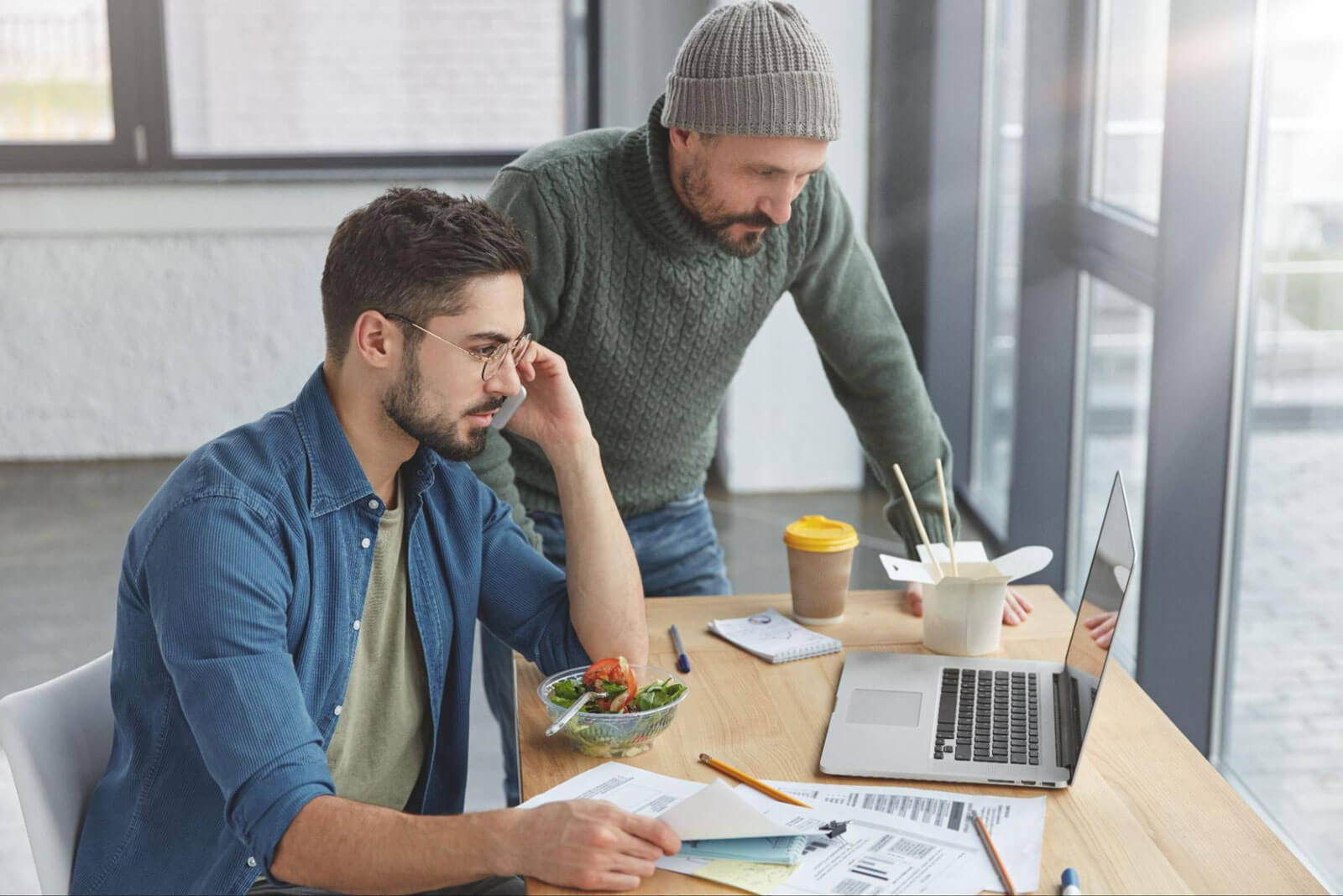Two men reviewing documents together at a table with a laptop, representing planning, guidance, and ongoing support in recovery or life transitions.