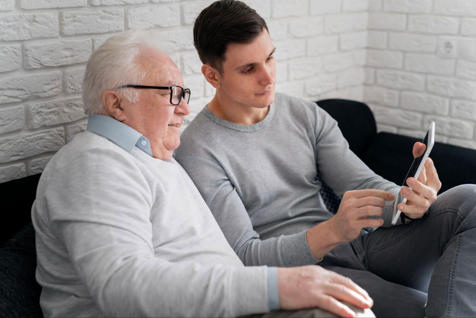 An older man and a younger man sitting side by side looking at a tablet, symbolizing mentorship, learning, and supportive connection.
