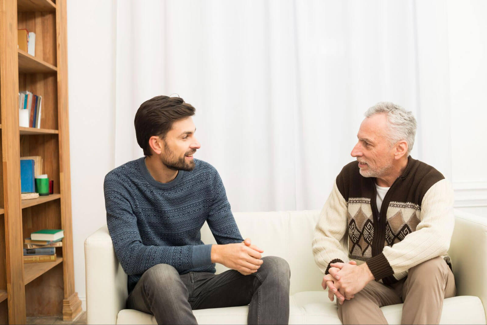 Two men sitting and talking face-to-face in a comfortable setting, reflecting open conversation, support, and personal growth.