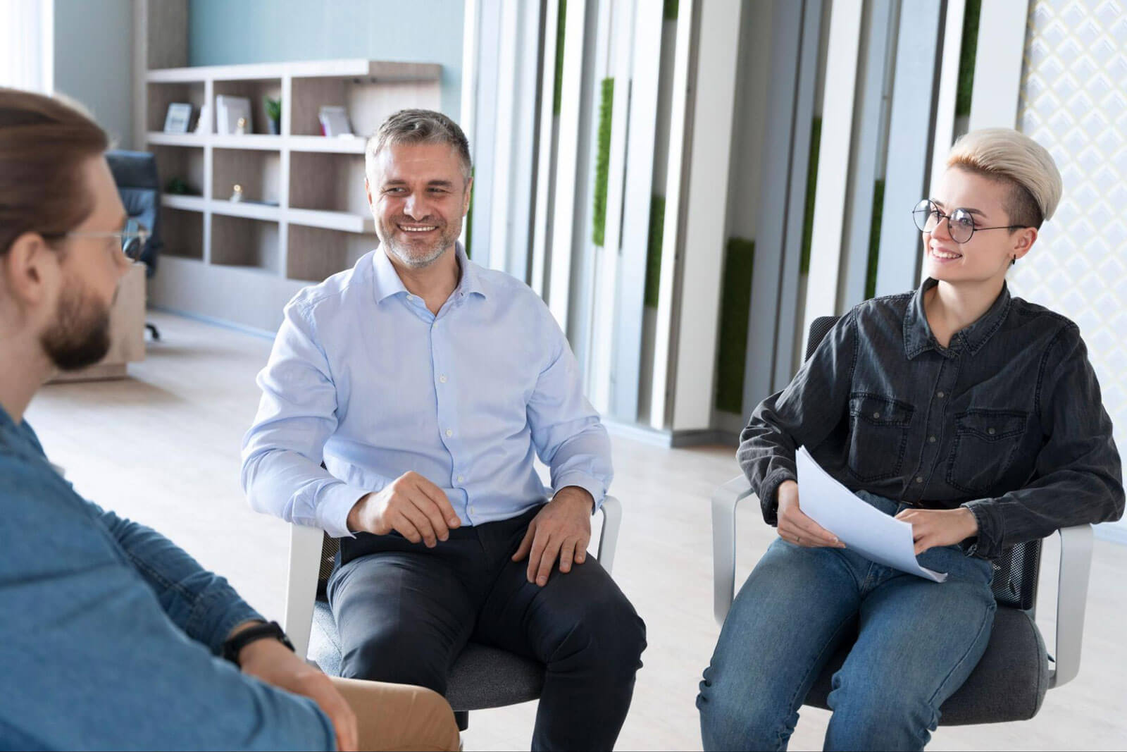 Three people sit together smiling in a bright modern office during a counseling conversation.