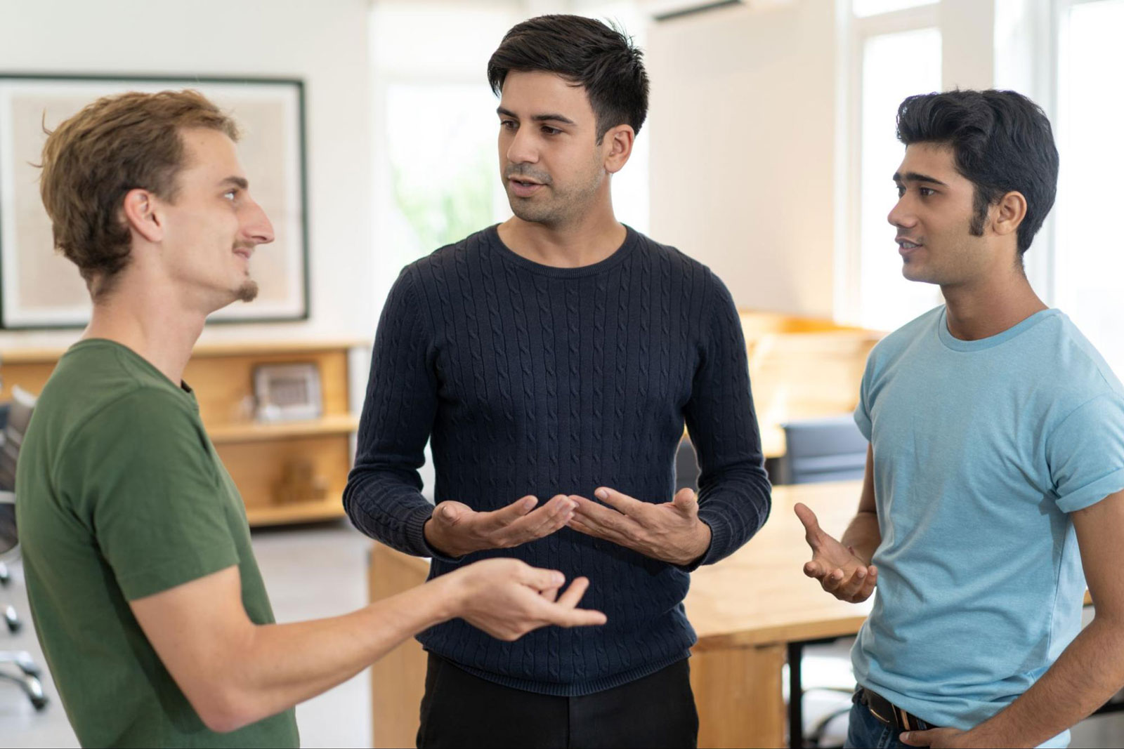 Three men have a supportive group discussion in a bright residential setting.